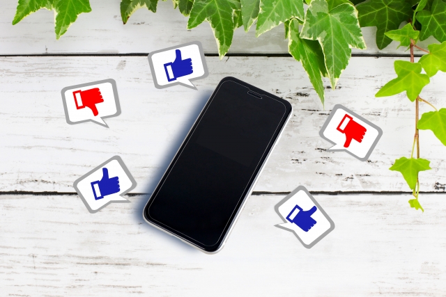 葉の垂れた壁の上のスマホとグッドボタンマークとバッドボタンマーク