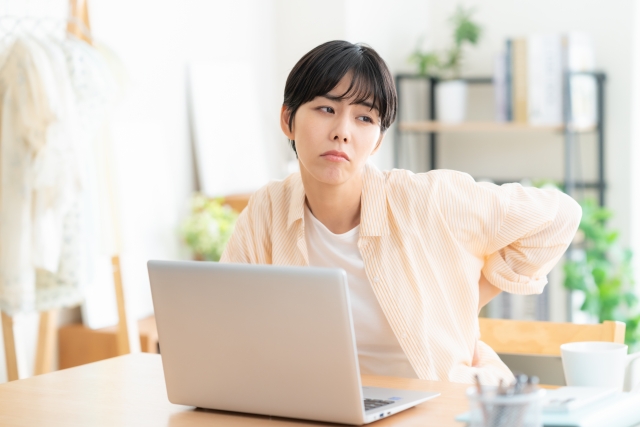 テーブルの上にあるPCを使っている女性が腰を押さえている