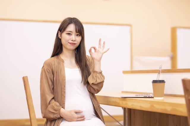 椅子に座ってOKサインを作る白いワンピースに茶色の羽織姿の妊婦