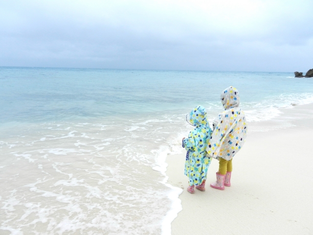 海でレインコートとポンチョを着ている子ども2人