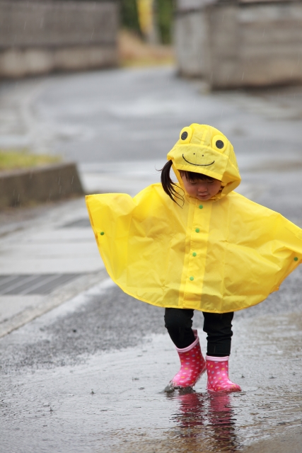 黄色のポンチョを着て水たまりで遊んでいる女の子