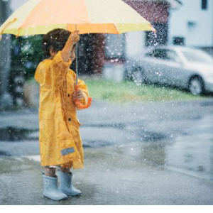 雨の日に黄色い傘とカッパと長靴を履いている男の子