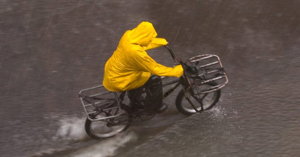 大雨の中を黄色いレインコートで自転車走行する人物
