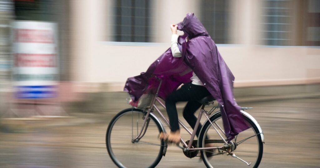 紫色のレインポンチョを着て雨の中を自転車で走る人物