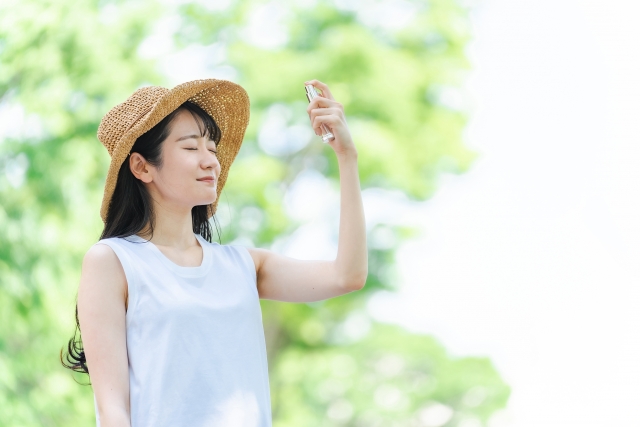 顔にスプレーをかける麦わら帽子をかぶった女性