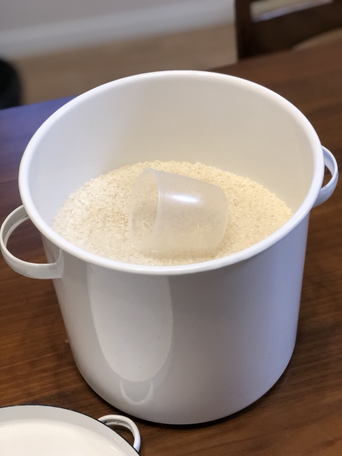 米と計量カップが入った白い米びつ