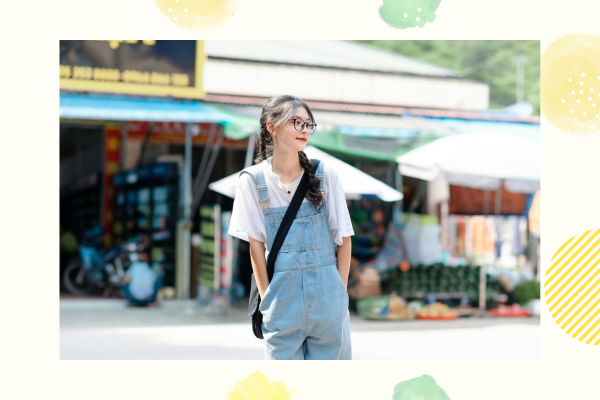 お店の前に立つデニムのオーバーオールを着た女性